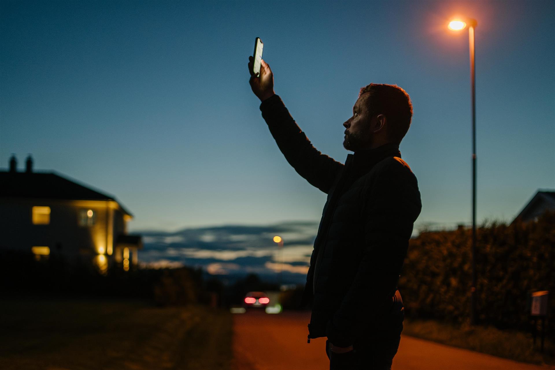 En mann holder mobilen sin opp i luften
